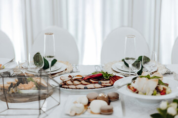A table with a variety of food and drinks, including a plate of meat, a bowl of salad, and a dessert plate with pastries. The table is set with white plates, silverware, and wine glasses