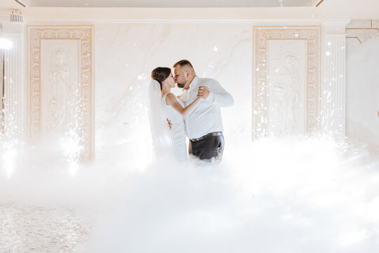 A bride and groom are dancing in a cloud of white smoke. Scene is romantic and playful - Powered by Adobe