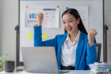 Happy asian businesswoman raising hands with victory smiling happily with laptop computer. The concept of success at work.