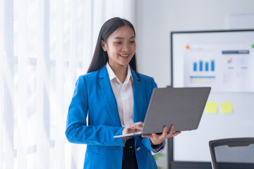 Successful Asian businesswoman smiling stand using laptop computer at office. Confident Asia businesswoman happily in the office.