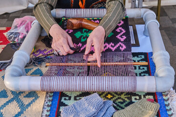 Hands of senior woman weaves a carpet with traditional asian pattern on handloom