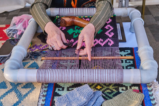 Hands of senior woman weaves a carpet with traditional asian pattern on handloom