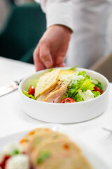 waiter holds a fresh Caesar salad with crispy lettuce, tomatoes, grilled chicken, and parmesan cheese in a white bowl