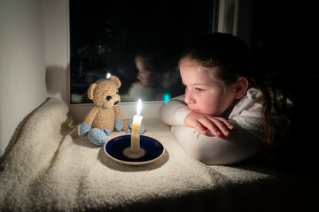 Blackout. A girl with a teddy bear in a dark room lies on the windowsill near the window and looks...