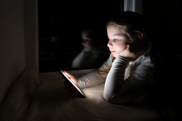 Blackout. A girl in a dark room lies on the windowsill near the window and uses a smartphone