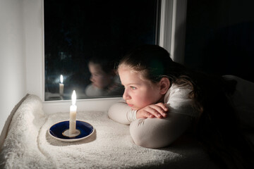 Blackout. A girl in a dark room lies on the windowsill near the window and looks at a burning candle