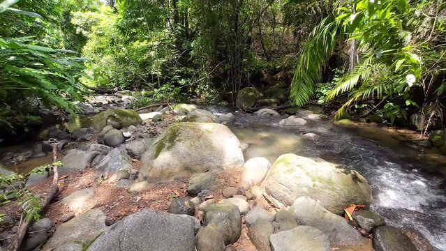 Gentle tracking shot through a picturesque river with majestic waterfall and large stones 4K resolution