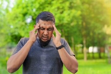 Closeup of young man suffering from headache at park, touching his temples, copy space, blurred...