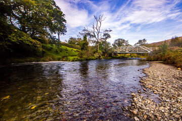 Obraz premium The clear water of the Aflon Glaslyn (River Glaslyn) with an Iron truss railway bridge in the background in Eryri National Park in Wales
