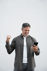 Happy delighted satisfied business man looking smartphone mobile phone gesturing yes winning pose, isolated background. Overjoyed excited businessman, doing winner gesture, reading good news. Vertical