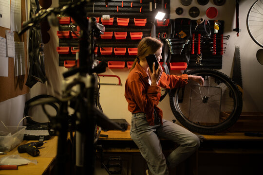 Bicycle maintenance and repair concept. Young blonde woman working in garage calling on mobile phone consulting with mechanic