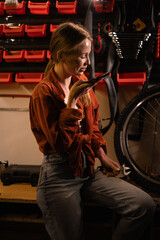 Young adult female repairing a bicycle in a bike workshop, dictate voice assistant, asking ai. Copy space