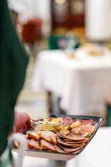 An attentive waiter in a fine dining setting, presenting a tray of assorted gourmet meats and condiments