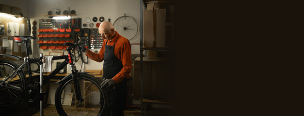 Old male mechanic doing his professional work in workshop or garage. Bike service, repair and...