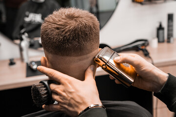 Barber cuts red-haired client occiput with adjustable trimmer in barbershop closeup. Professional master does masculine hairstyle to man in salon