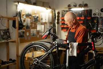 Bike service, repair and upgrade concept. Cycling mechanic fixing bicycle seat in workshop or garage. Old caucasian repairman.