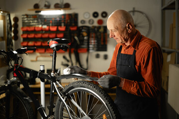 Bicycle Maintenance Concept. Old male mechanic or repairman working in a motorcycle repair garage, cleaning a wheel from dust.