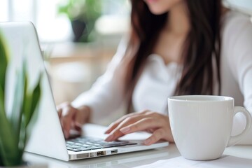  blur white office with a woman working on a laptop and coffee mug is in focus