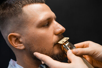 Young man undergoes mustache hair-cutting in luxury barber-shop closeup. Hairdresser uses shaver...