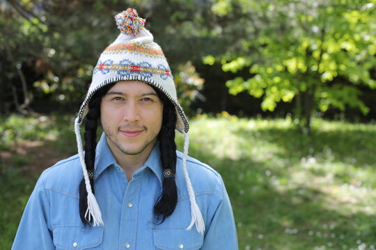 Young Man Wearing Traditional Andean Chullo Hat with Braids in Sunny Garden