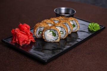 deep fried Japanese Sushi rolls with chopsticks and soy sauce on a black plate