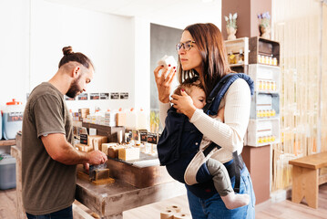 Mother Carrying Her Baby Smelling Artisan Soap At A Bulk Grocery Store