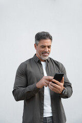Smiling hispanic business man using smartphone mobile phone device for online financial bank transactions. Freelancer entrepreneur in shirt holding cellphone isolated on white background, vertical