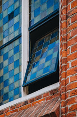 An open, small window with a stained glass window in a red brick building.   - 800385480