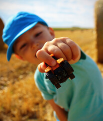 Happy 3-year old Caucasian boy showing a small tractor toy in stubble on a summer day. Concept for...