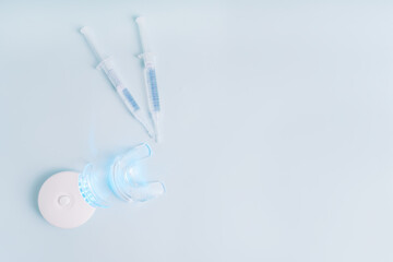Home portable equipment with blue light and syringes with teeth whitening product on blue background.