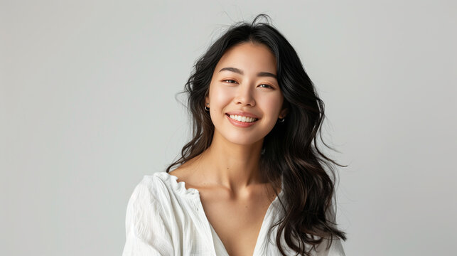 Portrait of a 30 year old Japanese woman smiling slightly on a grey background. Asian woman with a gentle smile and loose long hair in white shirt