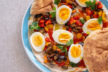 Traditional Israeli Sabich Salad including boiled eggs, pita bread, grilled eggplant, chopped vegetables, tahini sauce.