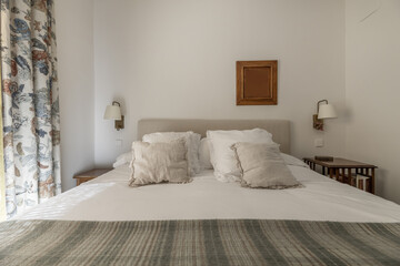 Double bedroom with fabric upholstered headboard and many cushions and pillows on the mattress