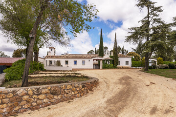 Dirt road leading to the main facade of a farmhouse with entrance to the property with white...