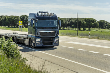 A tractor truck driving with an empty trailer on a county road