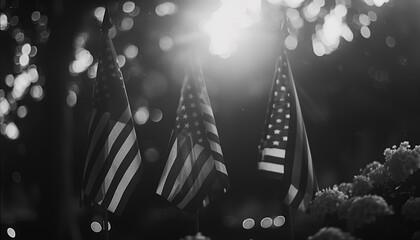 Black and white image of American flags fluttering, beautifully illuminated by soft bokeh lights in the background.
