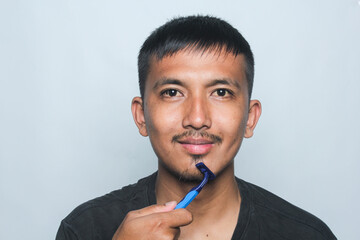 Asian young man being cut off beard and mustache isolated on white background.