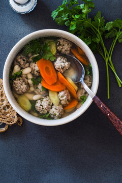 White bean and beef meatball soup with carrots on grey background, directly above