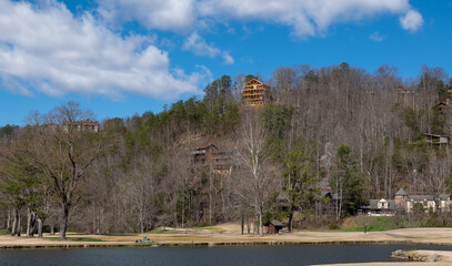 Several houses on the side of a hill with forest trees and a lake, on a beautiful spring day with blue sky and wispy white clouds.