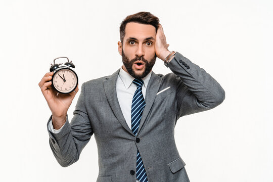 Surprised Caucasian businessman in formal suit holding clock isolated over white background. Time is up, deadline, hurry up, 5 minutes to New Year. Sale discount offer concept