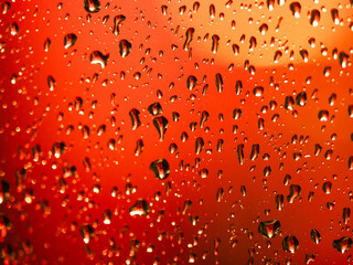 Raindrops on glass with orange background. Glass with water and colorful background. Rainy weather and macro drops .