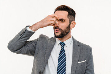 Displeased young businessman pinching his nose because of strong odor isolated over white...