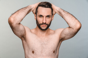 Sexy young naked man posing looking at the camera isolated over grey background. Handsome shirtless model touching his hair with good muscles body portrait