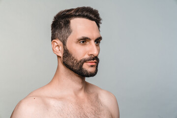 Side view portrait of young handsome man with beard naked isolated over grey background. Sexy attractive male model posing for barbershop salon, beauty care
