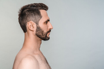Side view portrait of young handsome male model without clothes isolated over grey background....