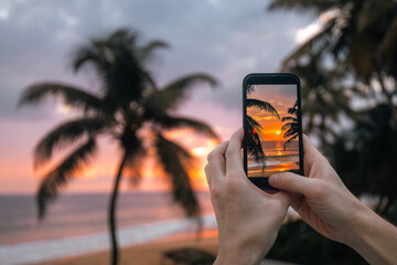 Close-up of hands holding smart phone. Man photographing sunset over ocean with mobile phone....
