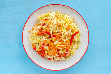 Coleslaw on ceramic plate over blue wooden background. Top view..