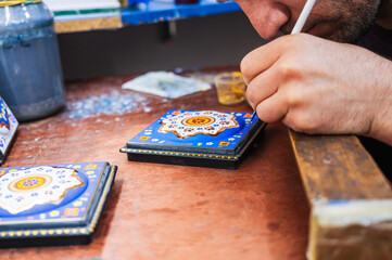 male artisan artist draws a pattern on a wooden casket with a brush in a workshop in Uzbekistan
