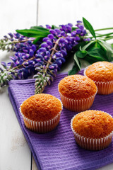 Freshly baked muffins and purple lupins on white wooden background. Homemade baking, preparing sweet dessert. Summer recipe. Vertical photo.