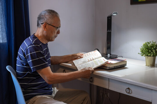 senior man learning new language, reading book, wearing glasses